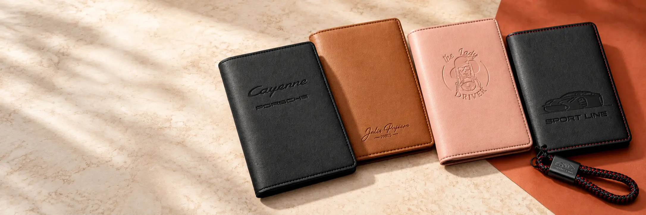 Étui Cayenne noir, protège-passeport camel Jolis Papiers, étui Lady Driver rose et ensemble Sport Line noir, dans une mise en scène beige et terracotta